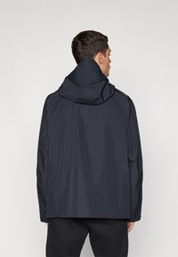 Marineblaue wasserdichte Jacke mit Kapuze, die eine glatte Textur und ein einfaches Design aufweist. Die Rückansicht zeigt keine zusätzlichen Details oder Verzierungen.