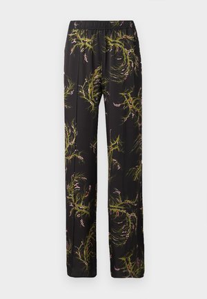 Kvinde iført sort ærmeløs top og sort viddebenet bukser med grønt og pink blomsterprint, stående med den ene hånd i lommen.