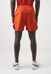 Orange shorts made of lightweight fabric with an elastic waistband and side pockets. The design includes a side slit for added mobility.