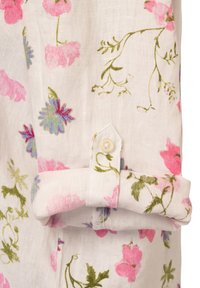 Blumenhemd mit pinkfarbenen und blauen Blumen auf einem weißen Leinenstoff, mit umgeschlagenen Ärmeln und einem kleinen Knopfdetail.
