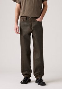 Temno zeleni, ohlapni kavbojke z gladko teksturo, pet žepov in svetlimi šivi. Obročene z sivo majico s kratkimi rokavi.