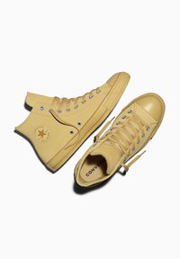Baskets montantes et basses jaunes en suède, avec des lacets, des semelles en caoutchouc, des œillets argentés et le logo de la marque sur le côté.
