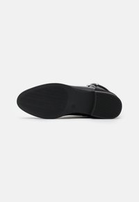 Semelle de chaussure noire en caoutchouc texturé, avec un motif de semelle et un bord lisse. Comprend une impression de logo près du talon.