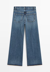 Niebieskie dżinsy z szerokimi nogawkami, z tylnymi kieszeniami, szlufkami na pasek i widocznym przeszyciem, ukazane od tyłu na białym tle.