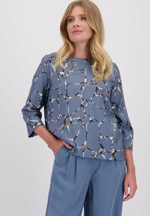 Blauwe top met een geometrisch patroon in tinten van bruin, lichtblauw, oranje en crème. Lange mouwen met een relaxte pasvorm en ronde halslijn.