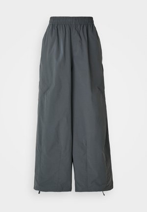 Grå, elastisk midjeband, vida byxor tillverkade av lätt tyg, med två sidofickor och justerbara dragsnören vid fickorna.