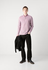 Svijetloljubičasta dugouhava polos majica s kontrastnim ovratnikom i tri gumba, uparena s crnim hlačama i tenisicama, drži crnu jaknu.