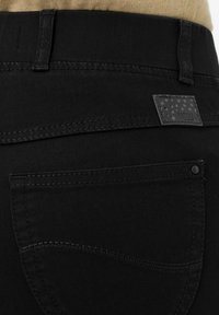 Jeans in denim nero con una tasca posteriore con cuciture sottili e un'etichetta nera rettangolare con un motivo a stella vicino alla vita.