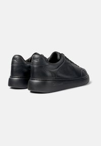 Black leather sneakers with a smooth finish, rounded toe, and a thick black rubber sole. Features subtle branding on the heel.