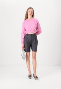 Rosa kort sweatshirt, grå tilpassede shorts, sølv håndveske, og grå sko med spisse tær. En enkel, moderne design med rene linjer.