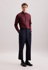 Bordeaux shirt met een puntige kraag, gecombineerd met marineblauwe, hooggetailleerde broeken. Zwarte schoenen maken de look compleet. Soepele stofstructuur.