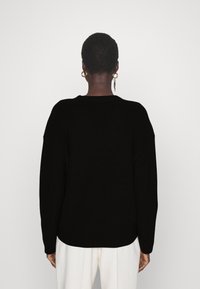 Svart stickad tröja med lös passform, vida ärmar och ribbad textur. Nederkant ligger strax under midjan och har inga synliga mönster eller detaljer.