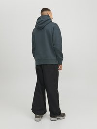 Mørkegrå hættetrøje med snøre, løs pasform og ribbede manchetter, kombineret med sorte brede bukser og grå sneakers.