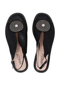 Schwarze Wildlederschlüpfschuhe mit rund ausgeschnittenem Design, das einen kreisförmigen metallischen Akzent und Strassdetails an der Oberseite aufweist.