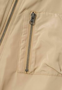 Giubbotto in nylon beige con zip, caratterizzato da una superficie liscia, una zip centrale e una tasca sul petto dotata di un tirazip argentato.