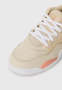 Zapatilla de cuero beige con cordones blancos, panel de malla y un acento coral en el lateral. Presenta una suela texturizada y un diseño de punta redonda.