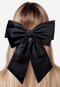 Black satin hair bow positioned at the back of long, straight blonde hair, featuring large loops and trailing ribbon ends.