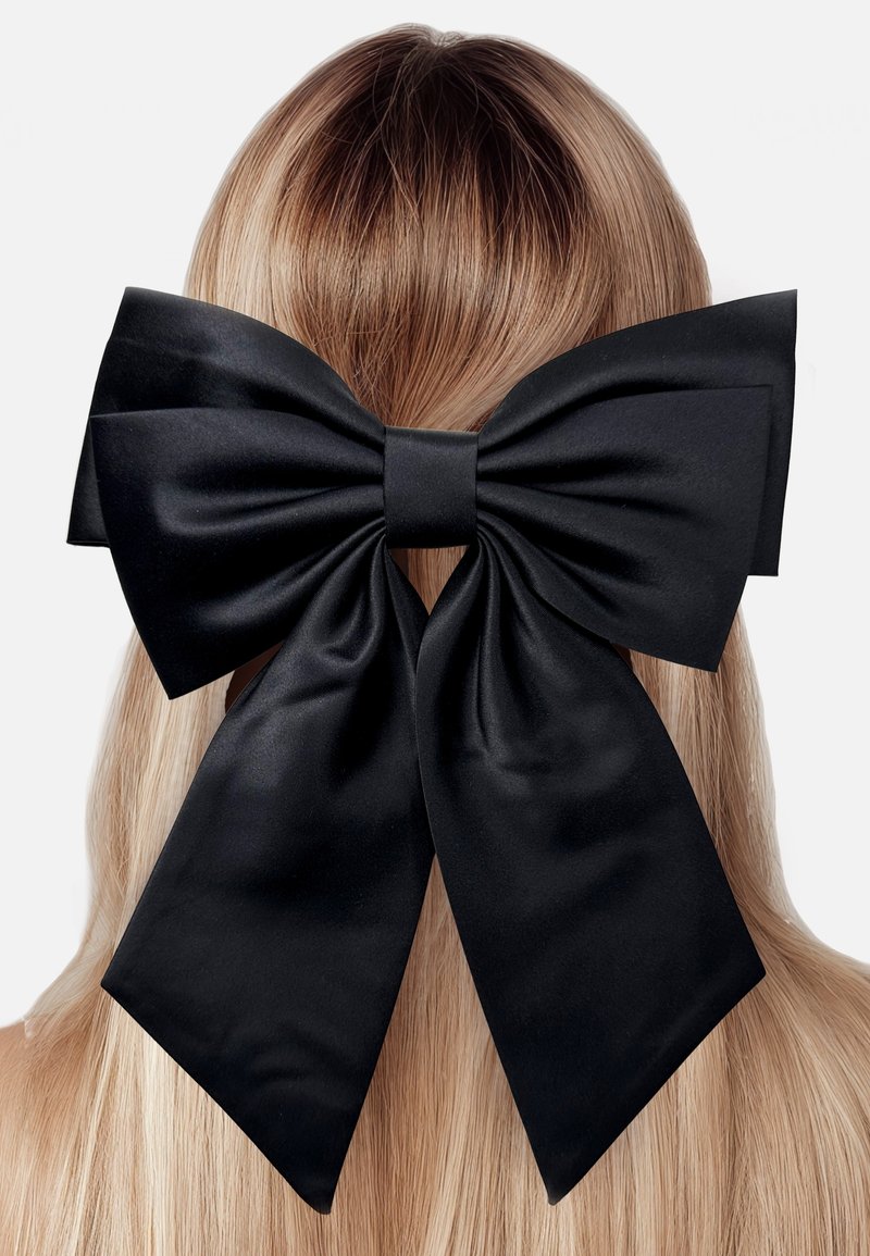 Black satin hair bow positioned at the back of long, straight blonde hair, featuring large loops and trailing ribbon ends.