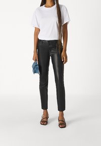 Svarta läderbyxor med slim fit, spetsat med en vit bomulls-t-shirt. Tillbehören inkluderar en blå tygclutch och svarta sandaler med remmar.