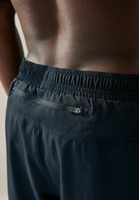 Shorts atletici negri cu talie elastică și o buzunar cu fermoar la spate. Țesătură netedă cu un ușor luciu.