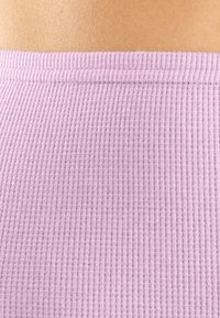 Gaiši rozā ribota auduma tekstūra ar rakstu, kas izceļ taisnu malu augšdaļā. Materiāls izskatās mīksts un elastīgs.