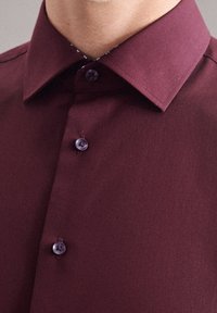 Burgundská košile na knoflíky s pevným límcem, hladkou strukturou a kontrastními detaily knoflíků, s jemným dekorativním vzorem uvnitř.
