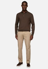 Brown knit polo shirt with a ribbed texture, three-button placket, paired with beige straight-leg trousers and brown suede sneakers.