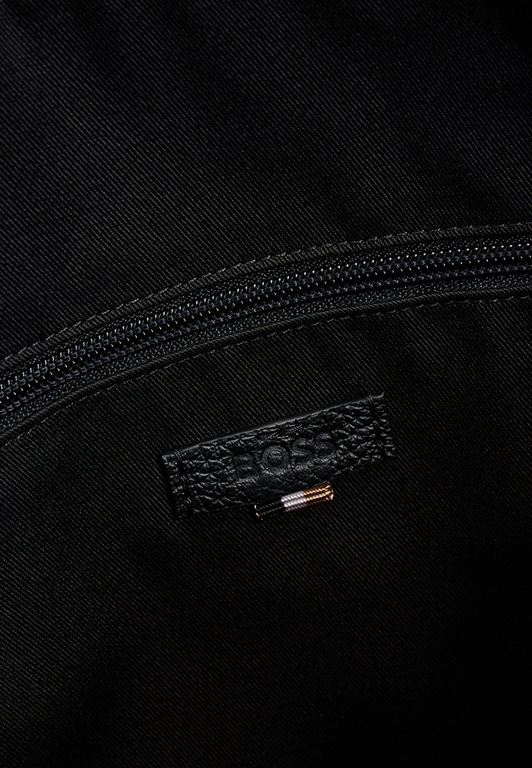 Sac en tissu noir avec une étiquette en cuir noir texturé portant le logo "BOSS." Comprend une fermeture éclair lisse noire en haut.