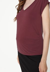 Top burgundy em V, feito de um tecido stretch suave, com franzido lateral e mangas curtas. Acompanhado de uma saia preta.