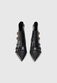 Botas negras de cuero hasta el tobillo con punteras afiladas, que cuentan con múltiples correas y hebillas, textura suave y cremalleras laterales para facilitar su uso.