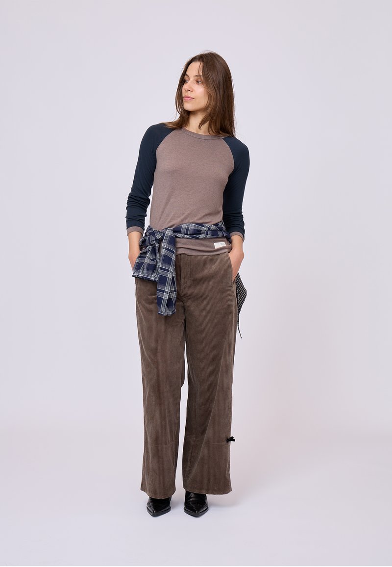 Pantaloni lunghi grigio-marrone con gambe larghe in tessuto di velluto a coste, abbinati a una maglietta a maniche lunghe beige e a una camicia a scacchi blu annodata in vita.
