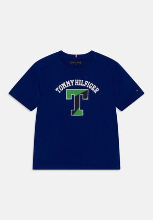 Granatowy T-shirt z krótkim rękawem z napisem „Tommy Hilfiger” i dużym zielono-czarnym logo litery „T” z przodu.