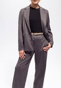Grauer, metallischer zwei-teiliger Anzug mit einem taillierten Blazer mit einem einzigen Knopf und weitem Hosenbein, kombiniert mit einem schwarzen Top und einem beigen Gürtel.