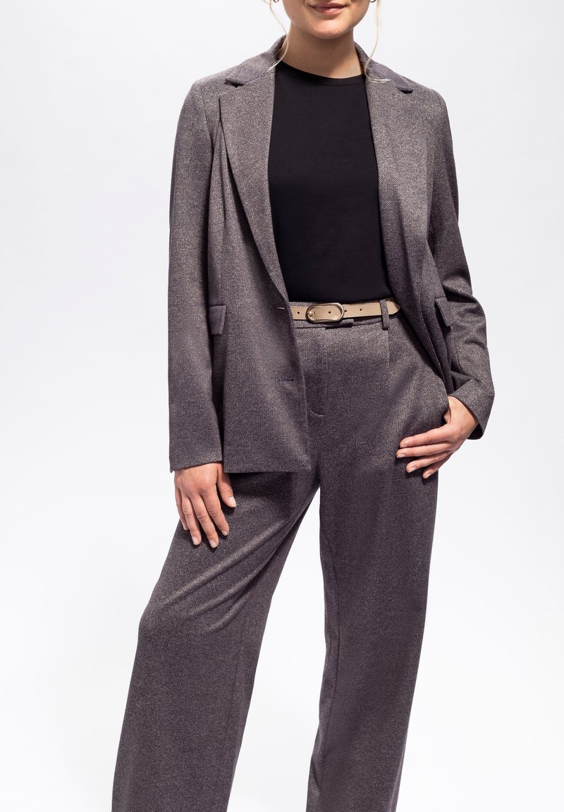 Grauer, metallischer zwei-teiliger Anzug mit einem taillierten Blazer mit einem einzigen Knopf und weitem Hosenbein, kombiniert mit einem schwarzen Top und einem beigen Gürtel.