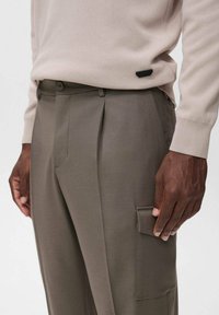 Lichtbeige trui gecombineerd met olijfgroene geplooide broek met een zijvak voor cargo, vervaardigd uit gladde stof met een getailleerde pasvorm.
