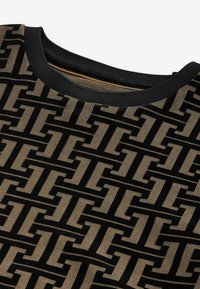 Tela negra con un patrón geométrico en beige, que presenta formas y texturas entrelazadas. Un cuello negro acanalado completa el diseño.