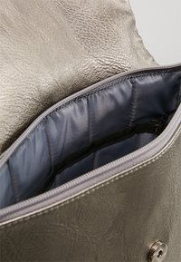 Vetoketjullinen pussi, jossa on tekstuurinen metallinen kultapinta ja sileä harmaa pehmustettu sisävuori, osittain avoinna näyttäen sisällä olevan mustan elastisen hihnan.