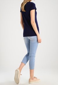 Námořnické tričko s krátkým rukávem, bavlněný materiál, těsný design. V kombinaci se světle modrými skinny džíny a béžovými teniskami, ukazuje módní outfit.