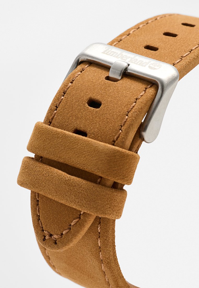 Tanjade suède horlogeband met dubbele lussen en een zilveren gesp met het Timberland-logo, op een witte achtergrond.
