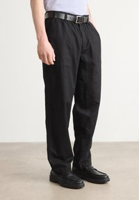 Black trousers with a loose fit, featuring side pockets and a textured fabric. Paired with a black leather belt and solid black shoes.