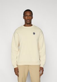 Μπεζ φούτερ από απαλό ύφασμα, με στρογγυλή λαιμόκοψη και ριμπς μανσέτες. Διακριτικό μαύρο κεντητό λογότυπο στο στήθος.