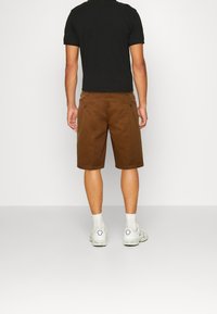 Hnědé šortky s rovný střih, se zadními kapsami, v kombinaci s černým tričkem a bílými teniskami, představují jednoduchý, ležérní vzhled.