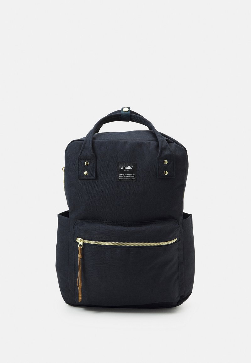 Sac à dos Anello noir avec poignées supérieures, une poche zippée à l'avant et deux poches latérales sur un fond clair uni.
