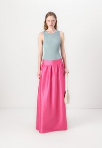 Top a maniche lunghe ribbed celeste abbinato a una gonna maxi in satin fucsia brillante, con una vita arricciata e una texture liscia. Tienendo in mano una borsa a tracolla beige.