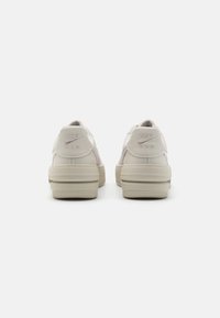 Nike Air sneakers in light beige leather. Features embossed logo at heel, textured accents, and a sturdy rubber sole with grip pattern.