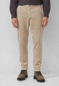 Beige Cordhosen mit geradem Schnitt, ausgestattet mit vertikalen Rippungen und einem Knopfverschluss. Kombiniert mit braunen Schnürstiefeln.