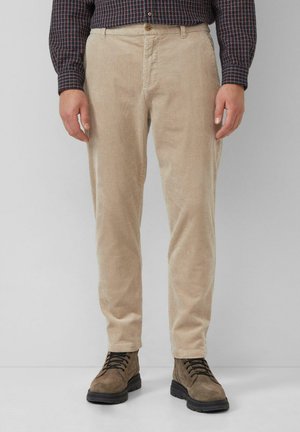 Pantalons en velours côtelé beige avec une coupe droite, présentant des côtes verticales et une fermeture à bouton. Associés à des bottes à lacets marron.