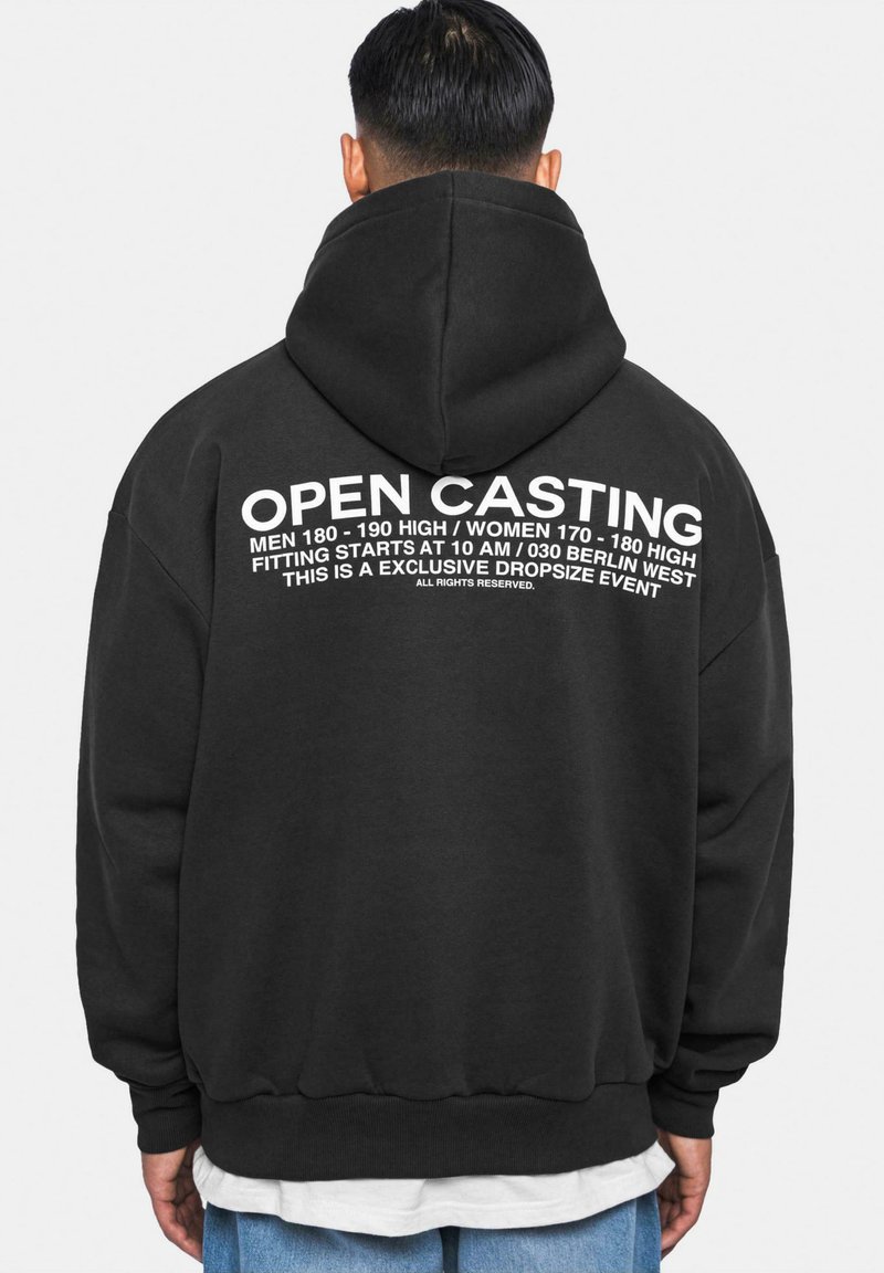 Schwarzer Kapuzenpullover mit großen weißen Schriftzügen auf dem Rücken, die "OPEN CASTING" und Einzelheiten zur Veranstaltung anzeigen. Weicher Stoff, lockere Passform.