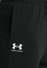 Schwarze Jogginghose aus weichem Material, mit Seitentaschen und einem weißen Under Armour-Logo auf dem linken Oberschenkel. Elastischer Bund für zusätzlichen Komfort.