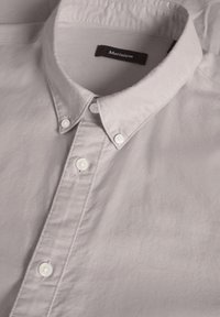 Cămașă de culoare gri deschis, cu nasturi, confecționată dintr-un material neted, având guler, nasturi albi și un etichetă cu "Matinique" pe dedesubt.